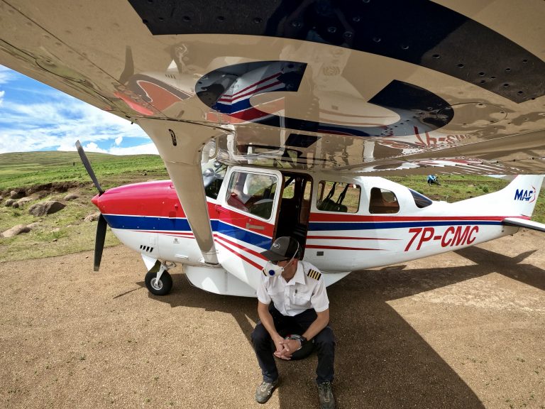 De afbeelding toont een MAF-piloot zittend in de schaduw van zijn MAF-vliegtuig.