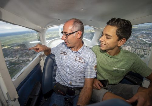 De afbeelding toont bezoekers in een vliegtuig die rondvliegen boven een stad op de vliegdagen.