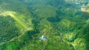 Blik vanuit de lucht op het groene landschap van Papoea-Nieuw-Guinea en de landingsbaan van Eliptamin waar een conferentie voor vrouwen heeft plaatsgevonden.